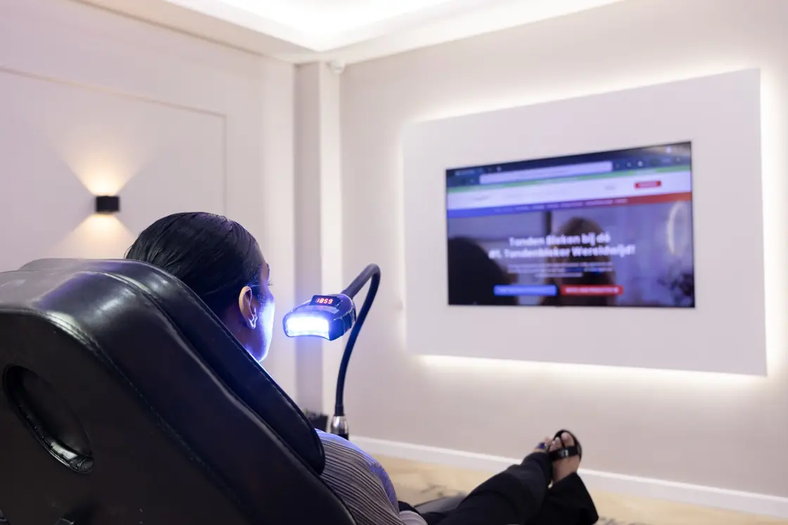 Klant ontspant in de behandelstoel met bleeklamp terwijl ze tv kijkt